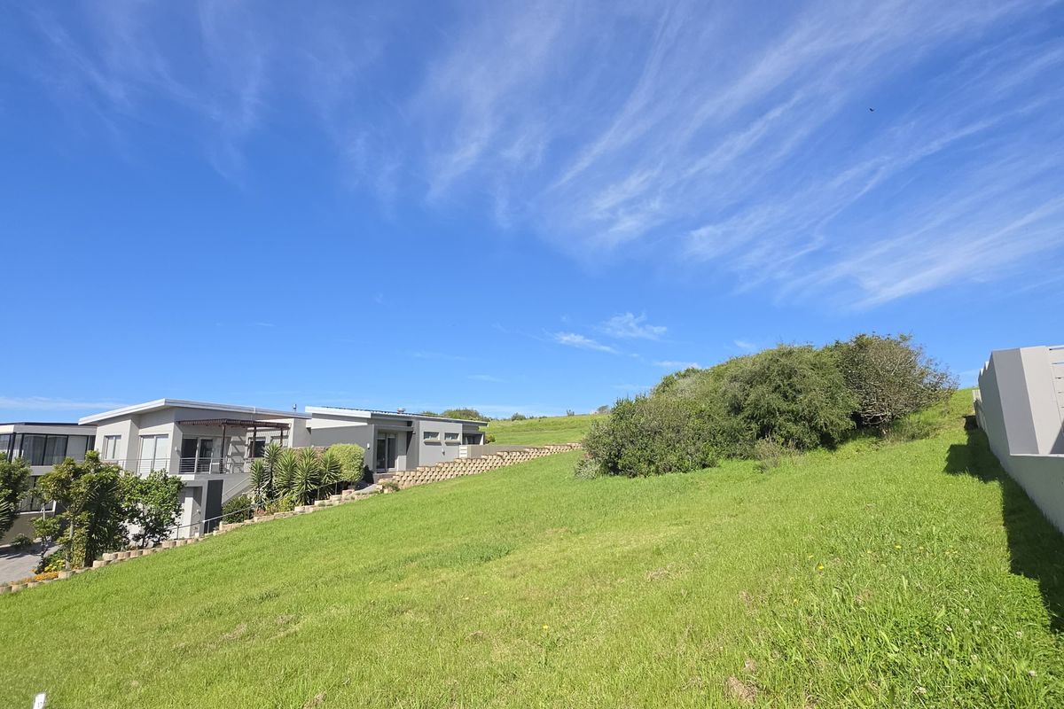 A view of a sloped residential vacant land plot featuring a retaining wall and adjacent modern housing.