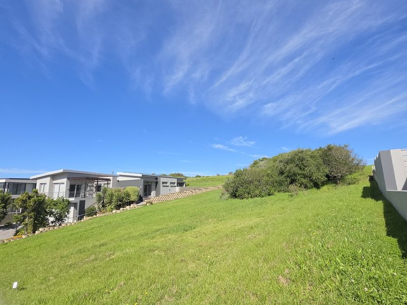 A view of a sloped residential vacant land plot featuring a retaining wall and adjacent modern housing.