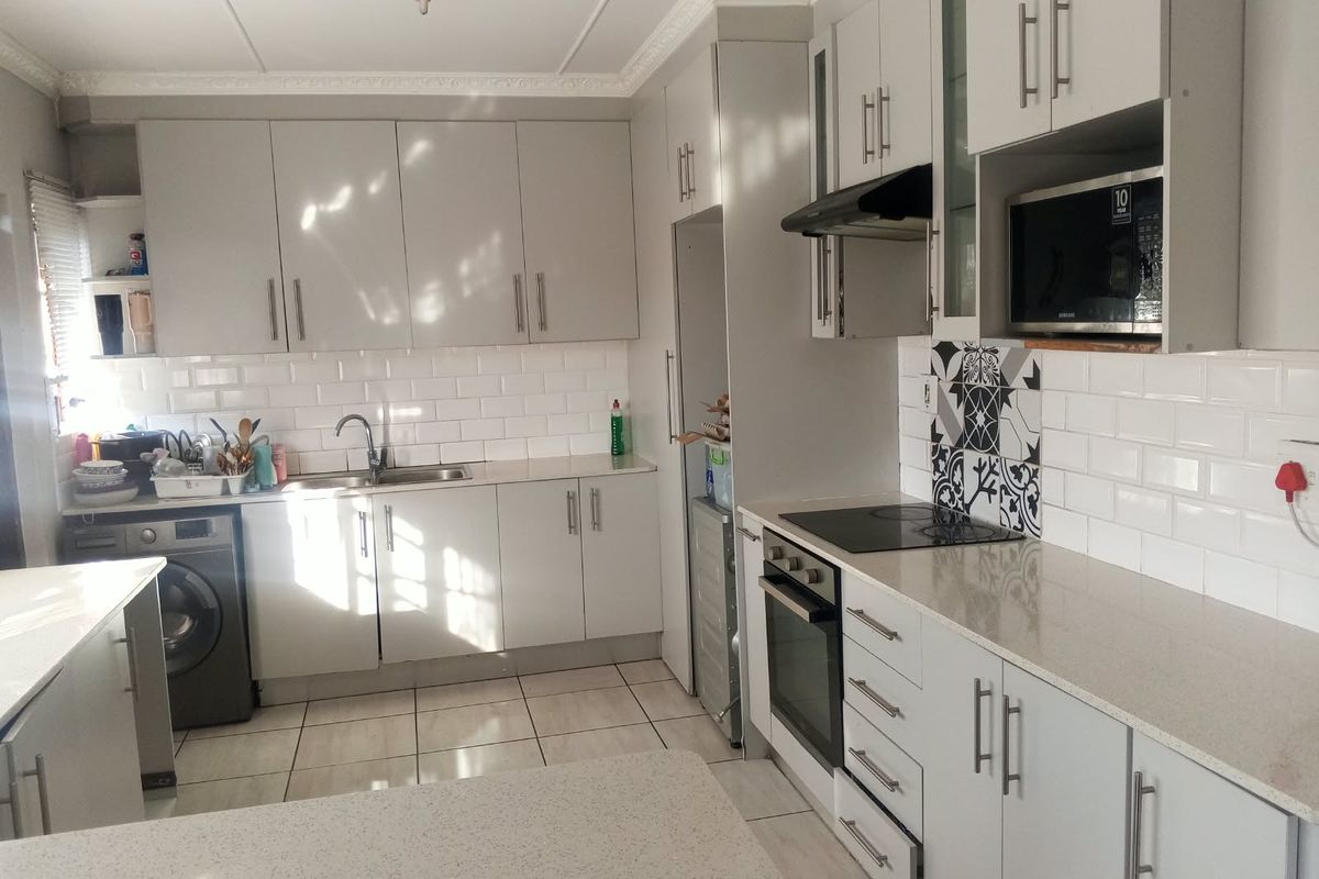 Modern kitchen featuring light grey cabinetry, stone countertops, subway tile backsplash, integrated oven, hob, and built-in microwave with tiled flooring.