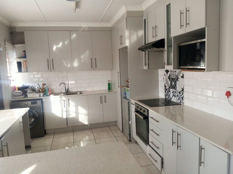 Modern kitchen featuring light grey cabinetry, stone countertops, subway tile backsplash, integrated oven, hob, and built-in microwave with tiled flooring.
