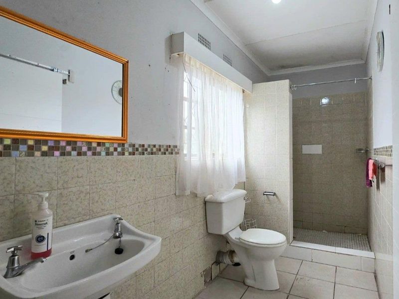 A functional bathroom featuring a walk-in shower, pedestal washbasin, and toilet, finished with ceramic wall and floor tiles and a decorative mosaic border.
