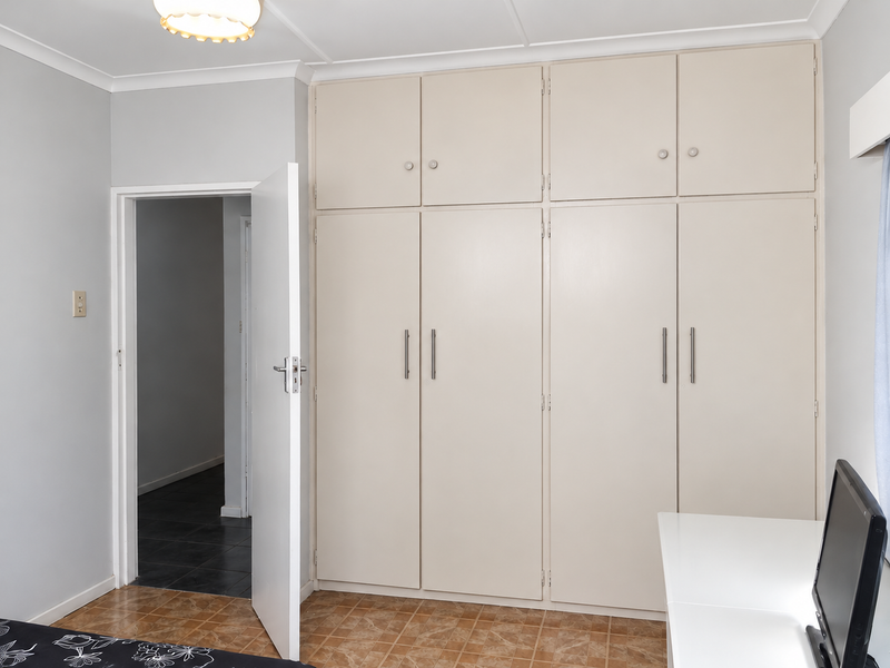 A bedroom featuring extensive built-in floor-to-ceiling cupboards, neutral wall finishes, and tiled flooring, providing ample storage space.