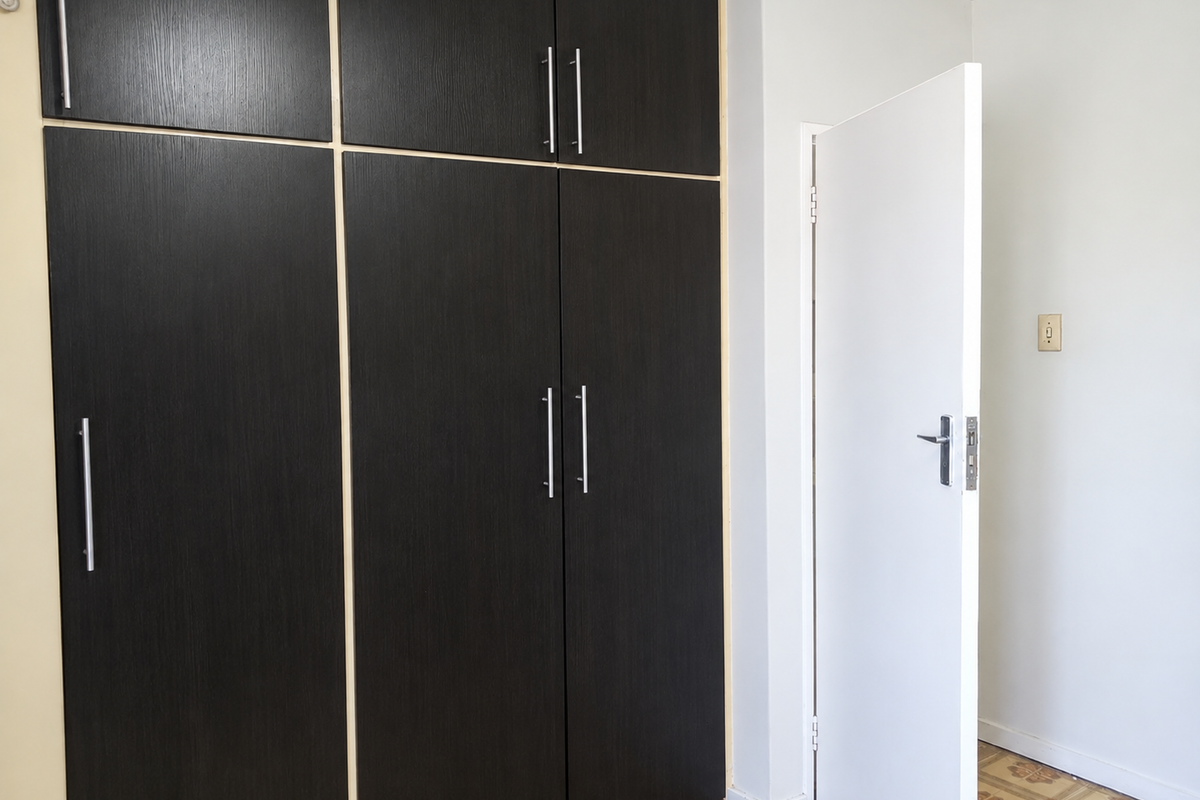 A bedroom featuring dark wood-finish built-in cupboards, tiled flooring, and a white internal door.