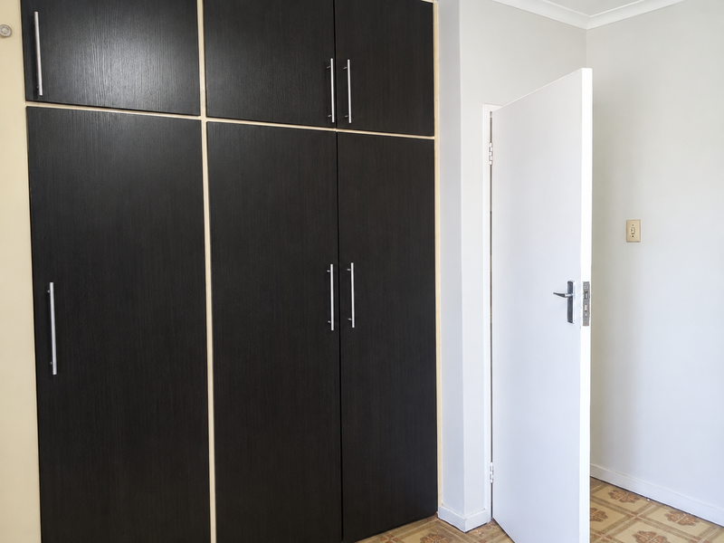 A bedroom featuring dark wood-finish built-in cupboards, tiled flooring, and a white internal door.