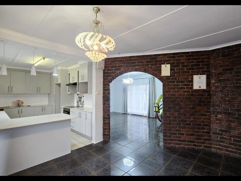 Open plan kitchen and living area featuring a distinctive exposed brick archway, modern cabinetry, tiled floors, and a breakfast island.