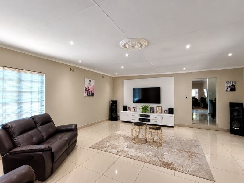 Spacious living room featuring polished tiled flooring, recessed downlighting, a decorative ceiling rose, and a modern built-in media wall unit.
