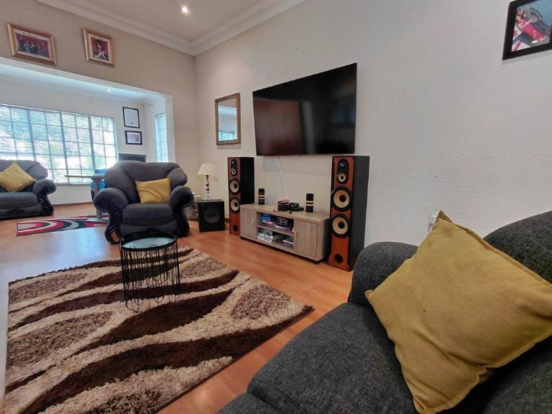 A comfortable living room featuring laminate flooring, coved ceilings, and recessed lighting, with an open-plan layout leading to an adjacent dining area.