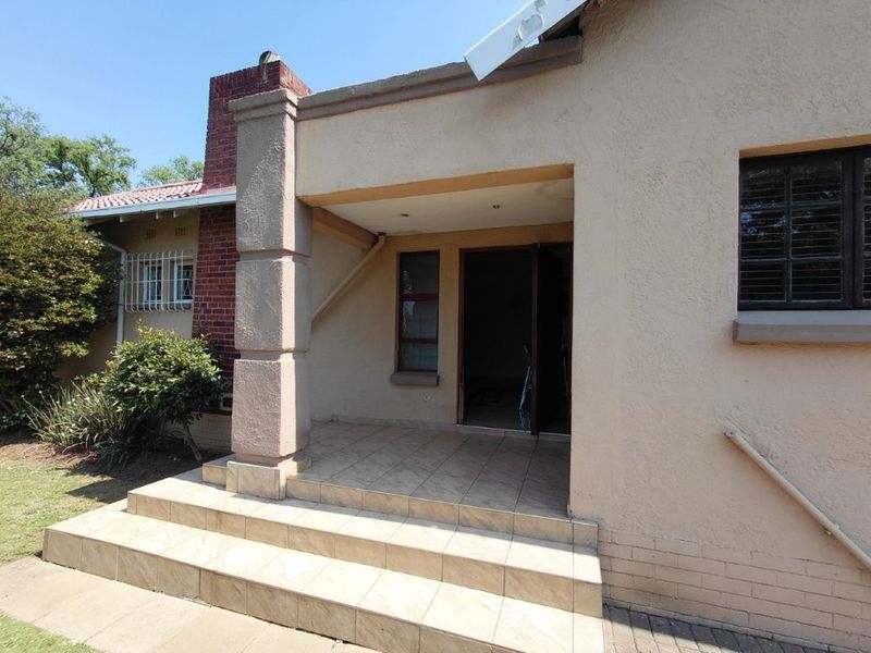A covered entrance patio featuring tiled flooring, a masonry pillar, and a brick chimney, providing access to the main interior living space.
