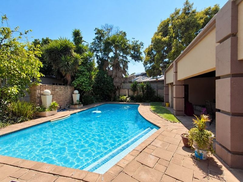 Outdoor pool area featuring a swimming pool, paved deck, stone feature wall, and a covered patio space.