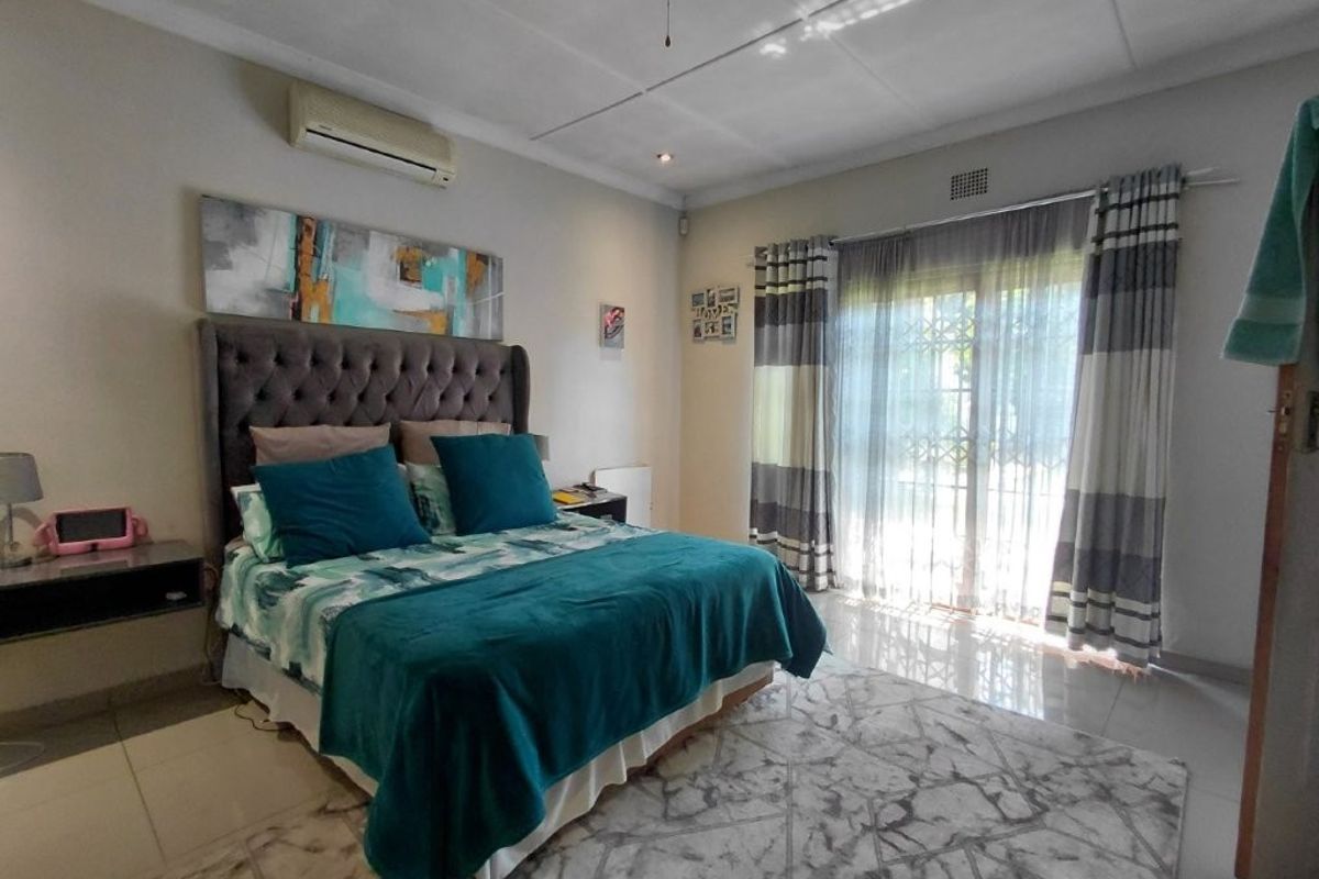 A well-maintained bedroom featuring tiled flooring, an air conditioning unit, and a sliding glass door with a security gate providing access to the outdoors.