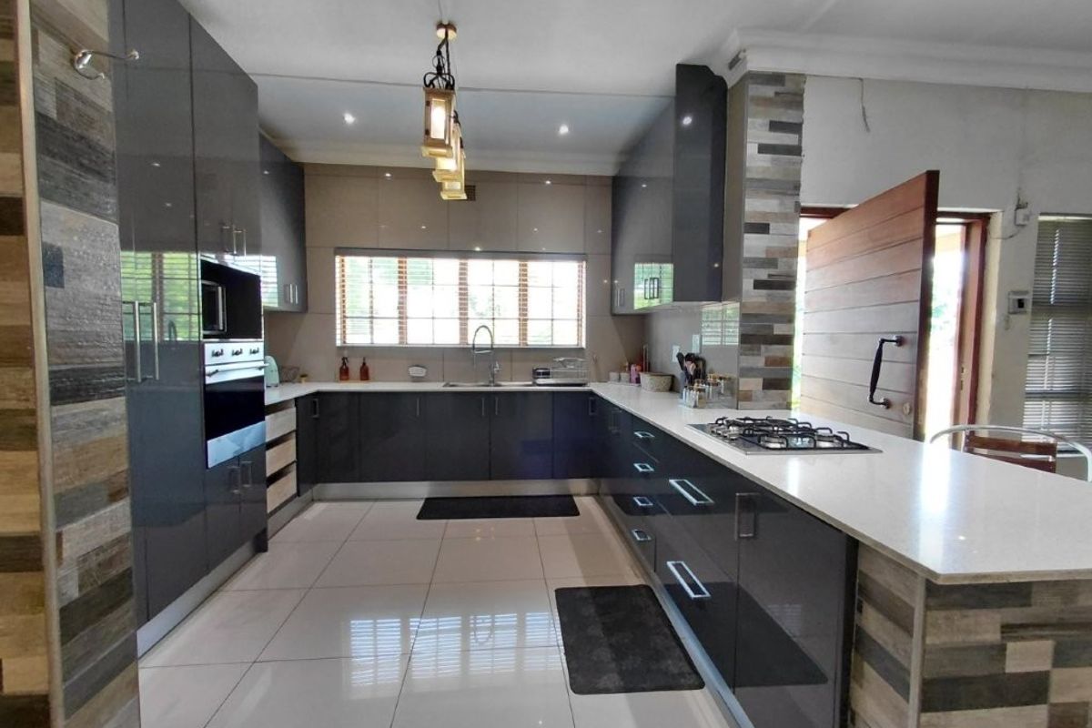 Modern kitchen featuring high-gloss cabinetry, stone countertops, built-in oven, gas hob, and stylish stone wall accents with polished tiled flooring.