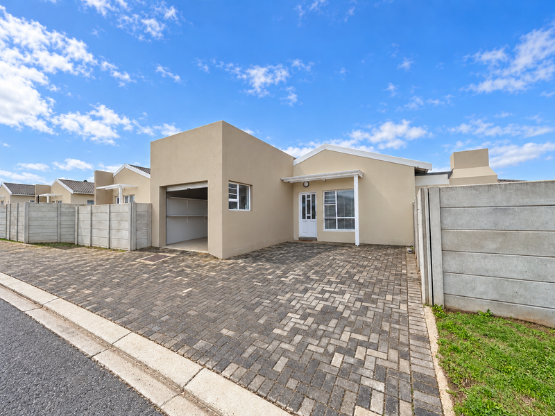 Front elevation of a modern single-story house featuring a paved driveway, integrated single garage, and secure precast concrete boundary walls.