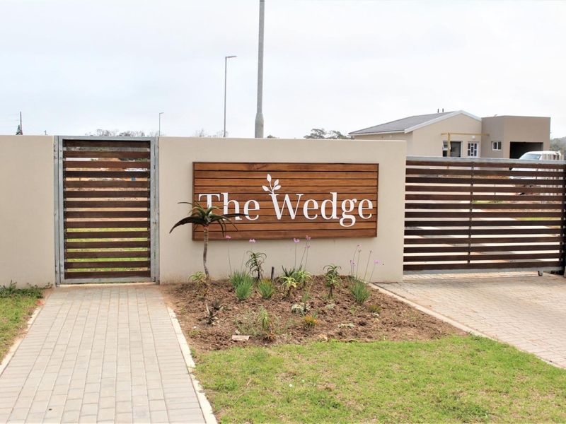 The entrance to The Wedge estate featuring a modern boundary wall, slatted metal gates, and a neatly paved driveway and walkway.