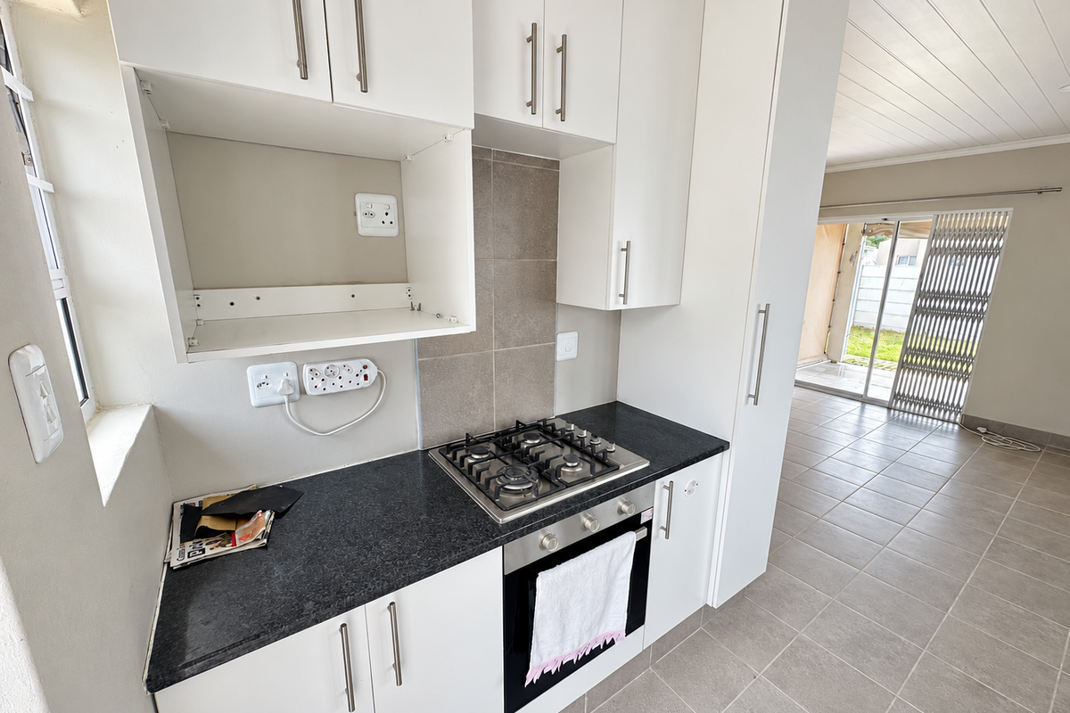 A clean, modern kitchen featuring white cabinetry, granite countertops, a gas hob, and a built-in oven, with tiled flooring and direct access to the patio.