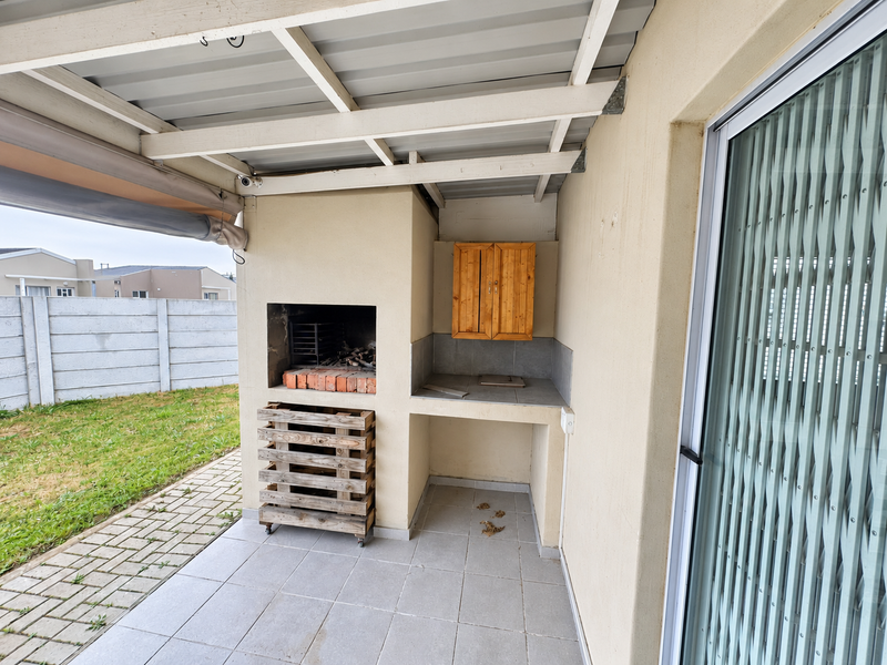Covered outdoor patio featuring a built-in braai, prep counter, and tiled flooring, providing a functional space for outdoor entertaining.
