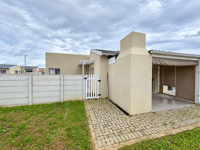 Rear exterior view featuring a paved patio area with an outdoor fireplace, enclosed by a precast boundary wall and a small pedestrian gate.