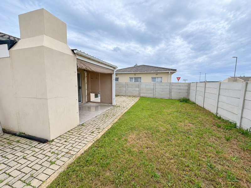 Rear garden area featuring a paved patio with an outdoor fireplace, retractable blind, and a secure precast concrete boundary wall.