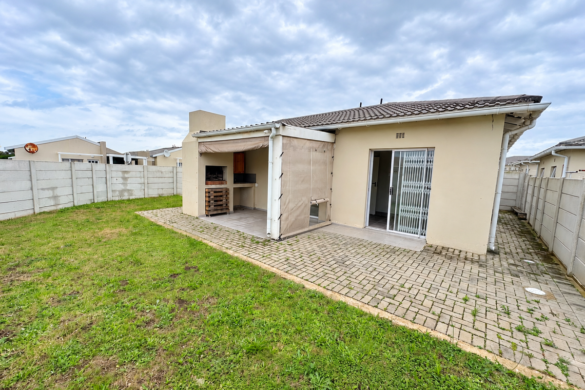 Rear view of the property featuring a paved patio area with a built-in braai, sliding door access, and a private garden enclosed by boundary walls.