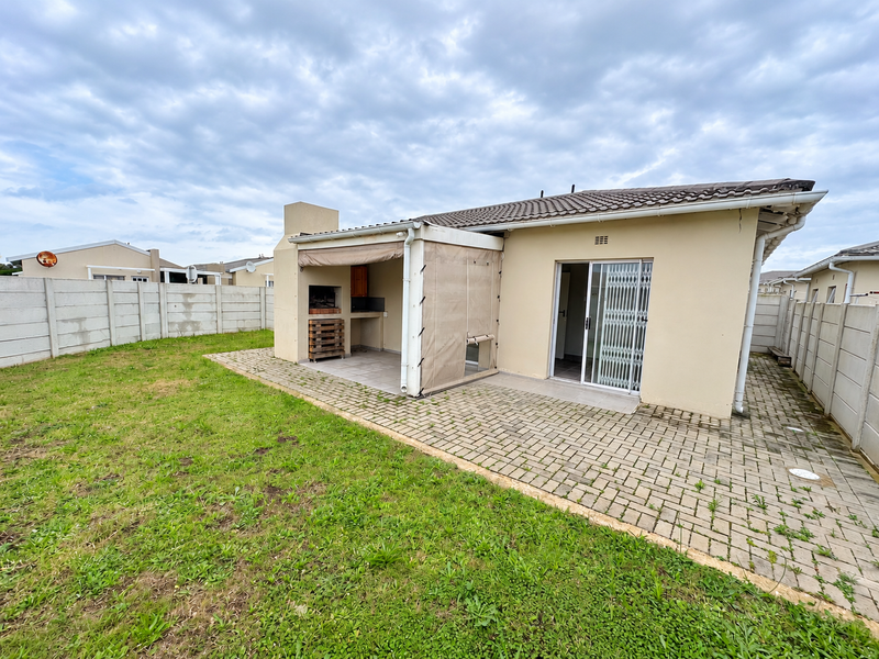 Rear view of the property featuring a paved patio area with a built-in braai, sliding door access, and a private garden enclosed by boundary walls.