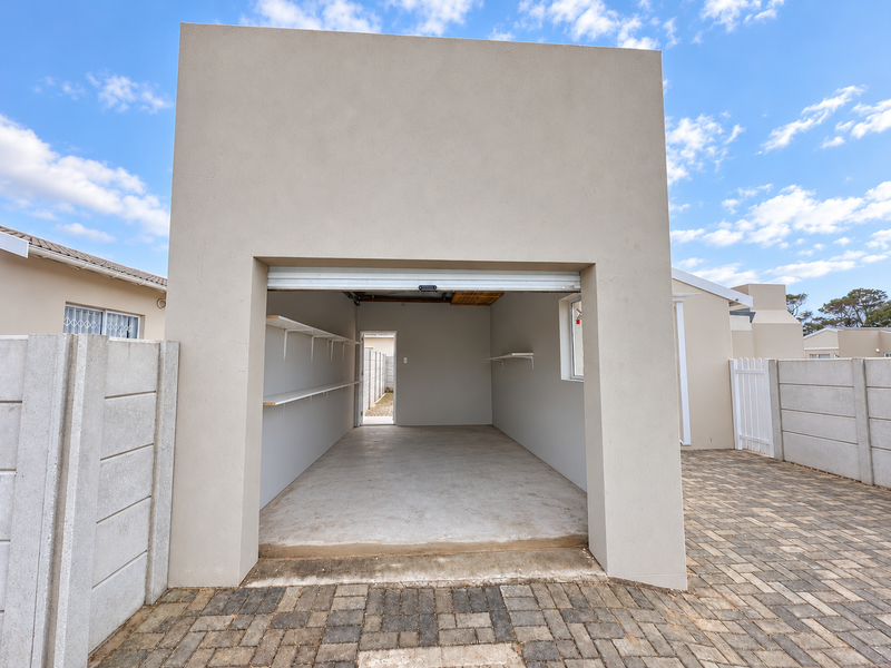 A clean, well-maintained single garage featuring concrete flooring, wall-mounted shelving, and a roll-up door, set within a paved courtyard area.