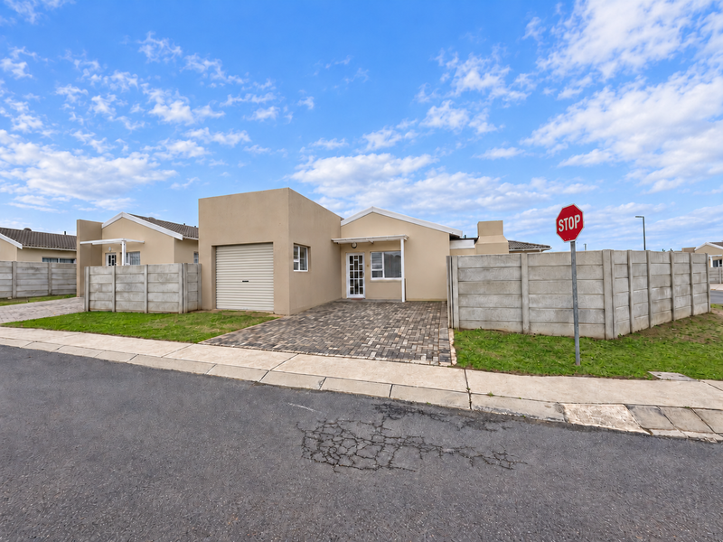 Front view of a modern single-story house featuring a paved driveway, integrated garage, and secure precast concrete boundary walls.
