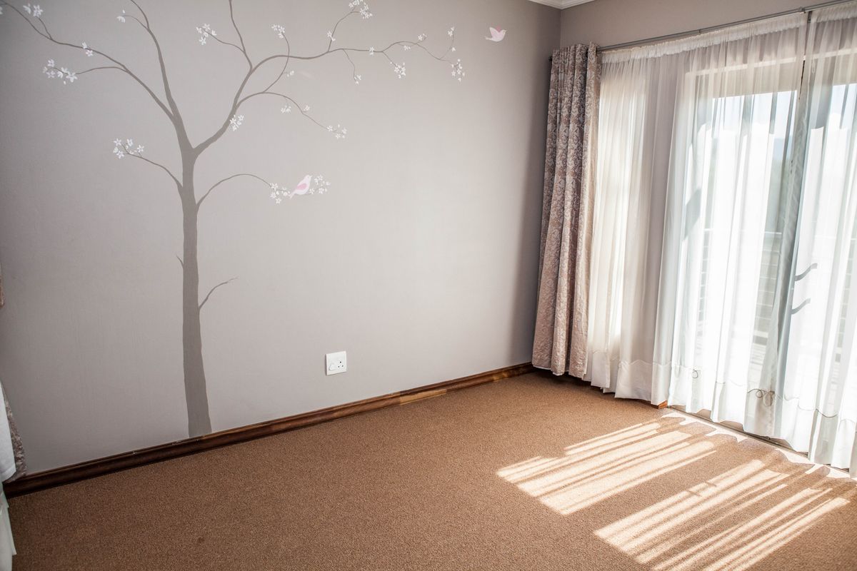 A bright, empty bedroom featuring neutral wall paint with a decorative tree mural, carpeted flooring, and a sliding glass door providing natural light.