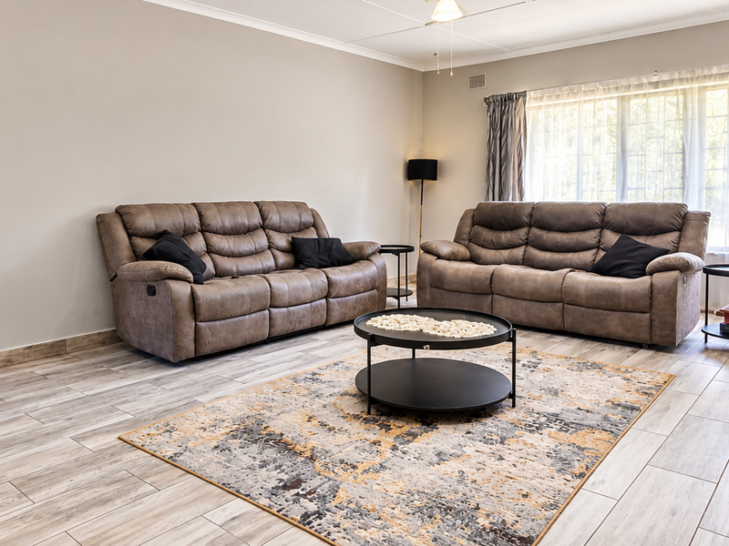 A spacious living room featuring modern wood-look tiled flooring, a stone-clad fireplace, and large windows that provide ample natural light.
