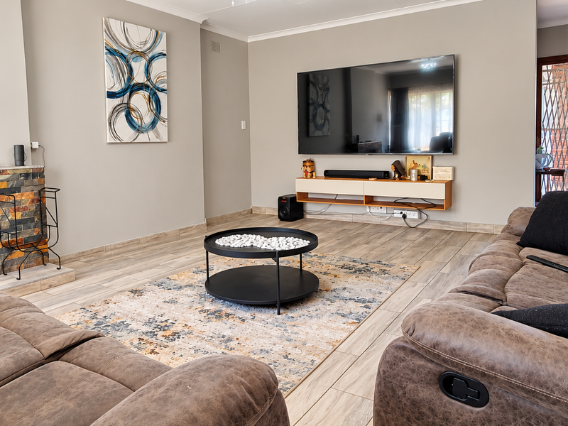 A well-maintained living room featuring wood-look tile flooring, a stone-clad fireplace, and a floating media console, leading to an outdoor area.