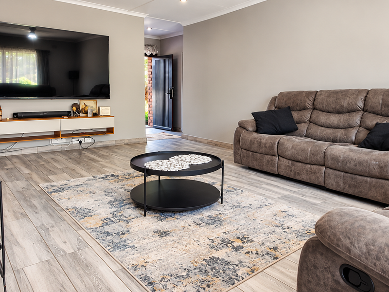 A well-maintained living room featuring wood-look tile flooring, a stone fireplace, and neutral wall tones, providing a comfortable and inviting space.