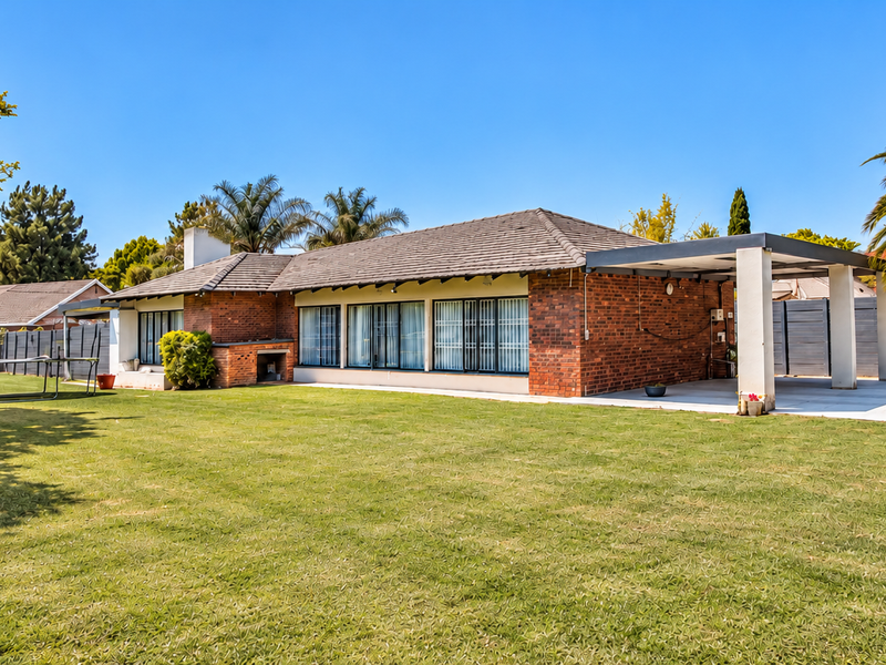 Spacious rear garden featuring a brick-faced house with a covered patio, built-in braai area, and a large lawn.