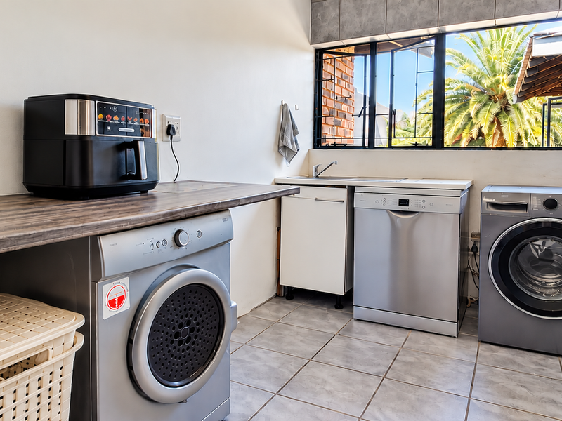 Functional laundry area featuring a laminate countertop, stainless steel sink, tiled flooring, and dedicated space for multiple appliances with natural light.