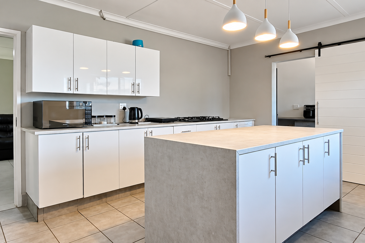 Modern kitchen featuring a central island, white cabinetry, gas hob, and a sliding barn door, complemented by neutral tiled flooring and pendant lighting.
