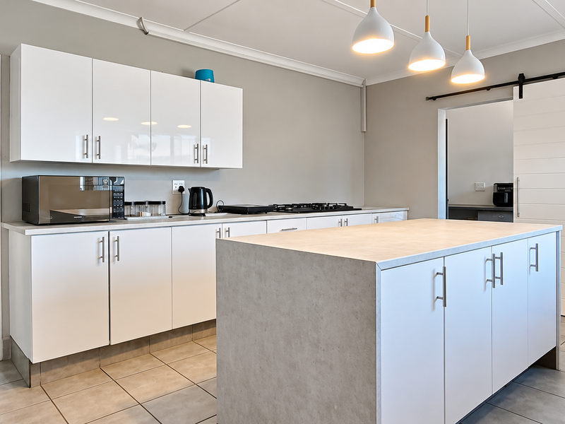 Modern kitchen featuring a central island, white cabinetry, gas hob, and a sliding barn door, complemented by neutral tiled flooring and pendant lighting.