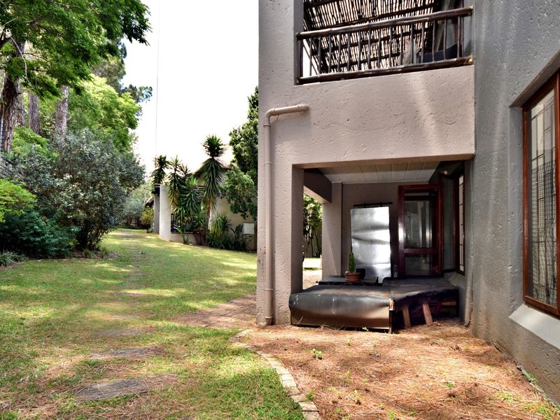 Rear view of the apartment featuring a covered ground-floor patio, an upper-level balcony with thatched roofing, and access to a shared garden area.