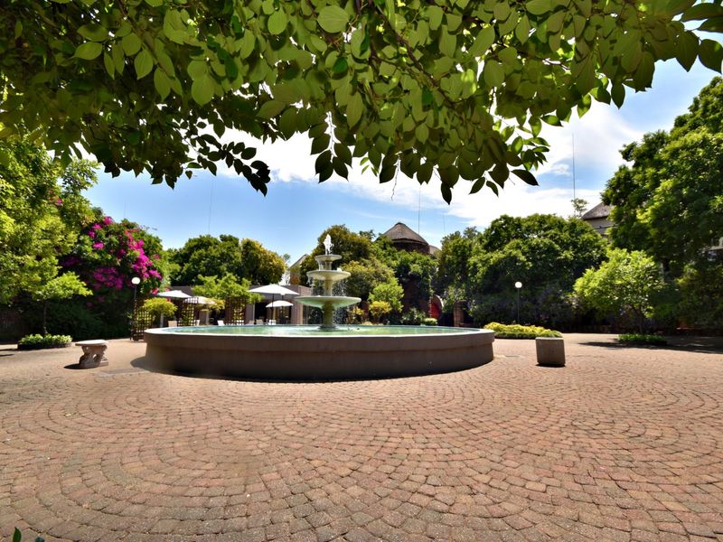 A well-maintained communal garden area featuring a central stone fountain and paved courtyard surrounded by mature trees and landscaped greenery.