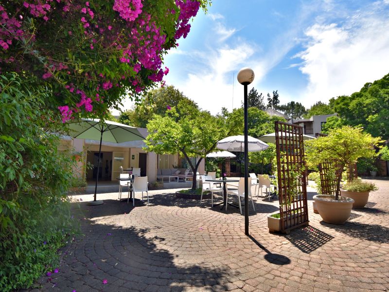 A well-maintained paved outdoor courtyard area featuring mature landscaping, established trees, and decorative trellis elements, providing a pleasant communal or private outdoor space.