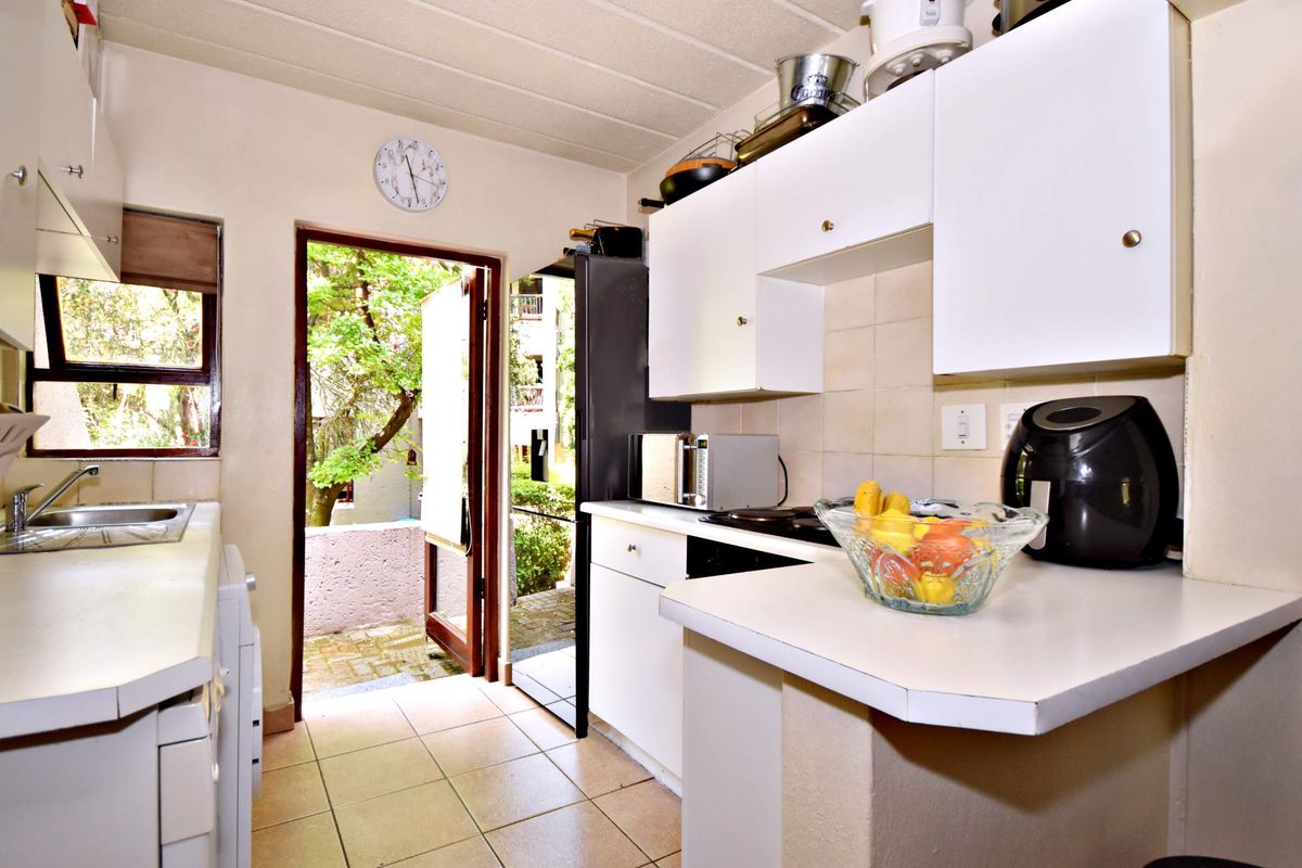 A functional kitchen featuring white cabinetry, tiled flooring, and direct access to an outdoor area, offering potential for modern updates.