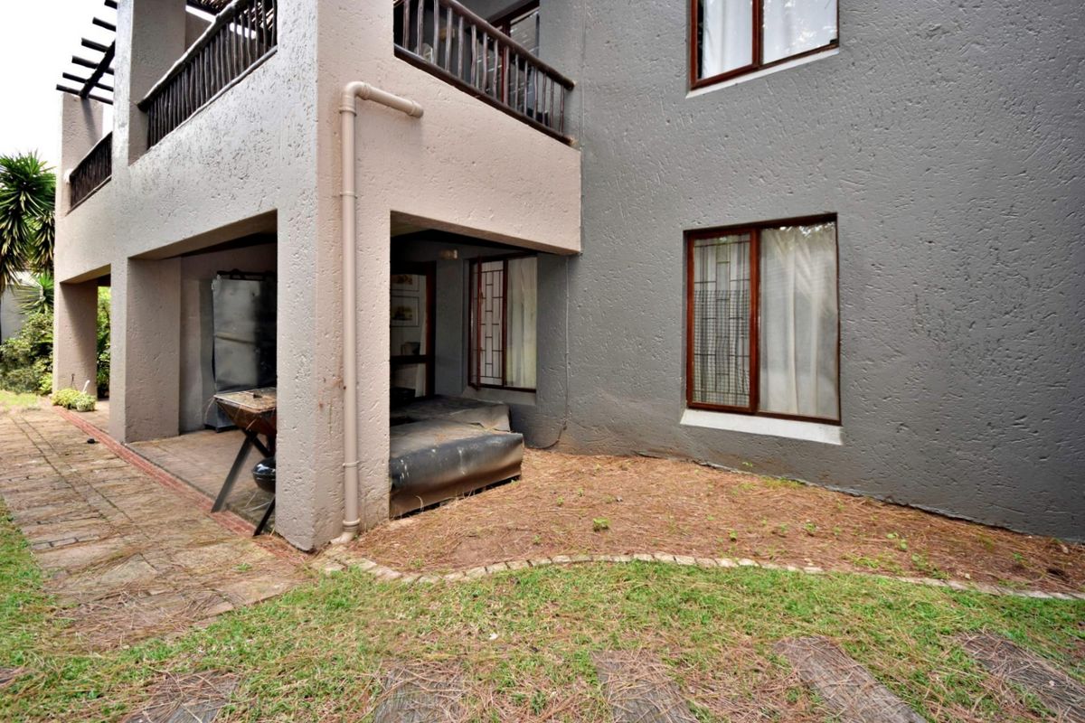 Rear view of the apartment building featuring a covered patio, balcony with timber balustrades, and a paved garden area.