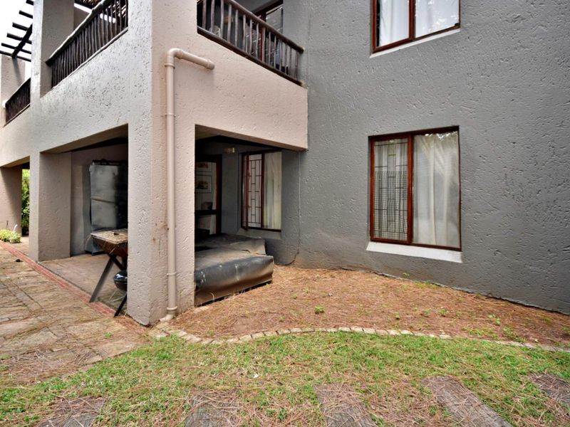 Rear view of the apartment building featuring a covered patio, balcony with timber balustrades, and a paved garden area.