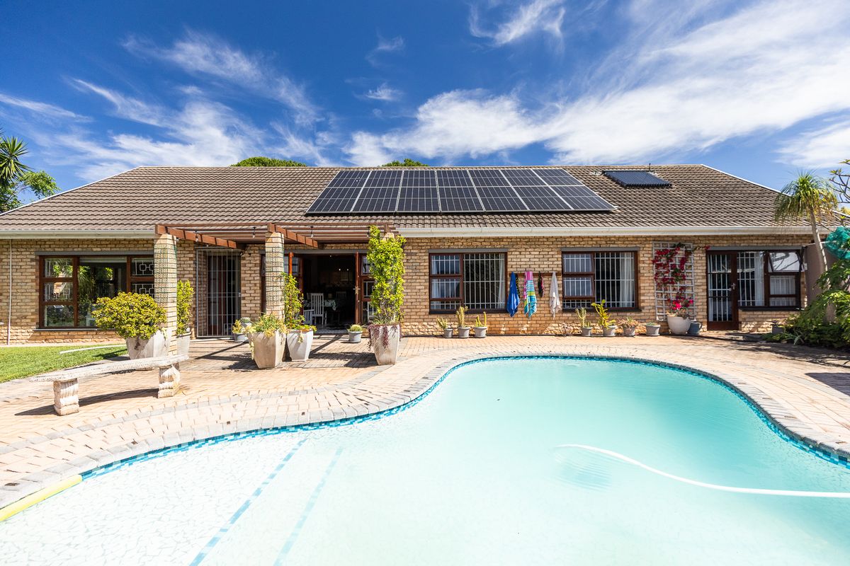 Rear exterior view featuring a swimming pool, paved patio area, pergola, and roof-mounted solar panels on a brick-faced house.