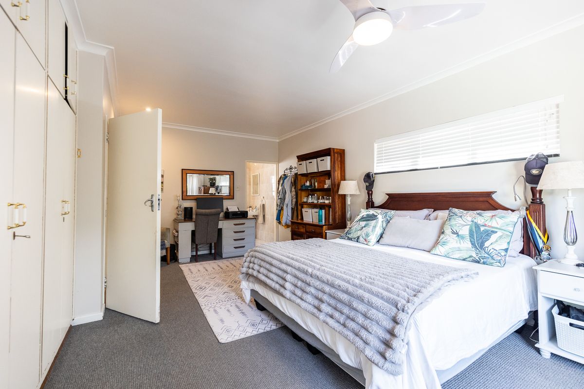 A well-maintained bedroom featuring built-in cupboards, a ceiling fan, and neutral carpeted flooring with access to an en-suite bathroom.