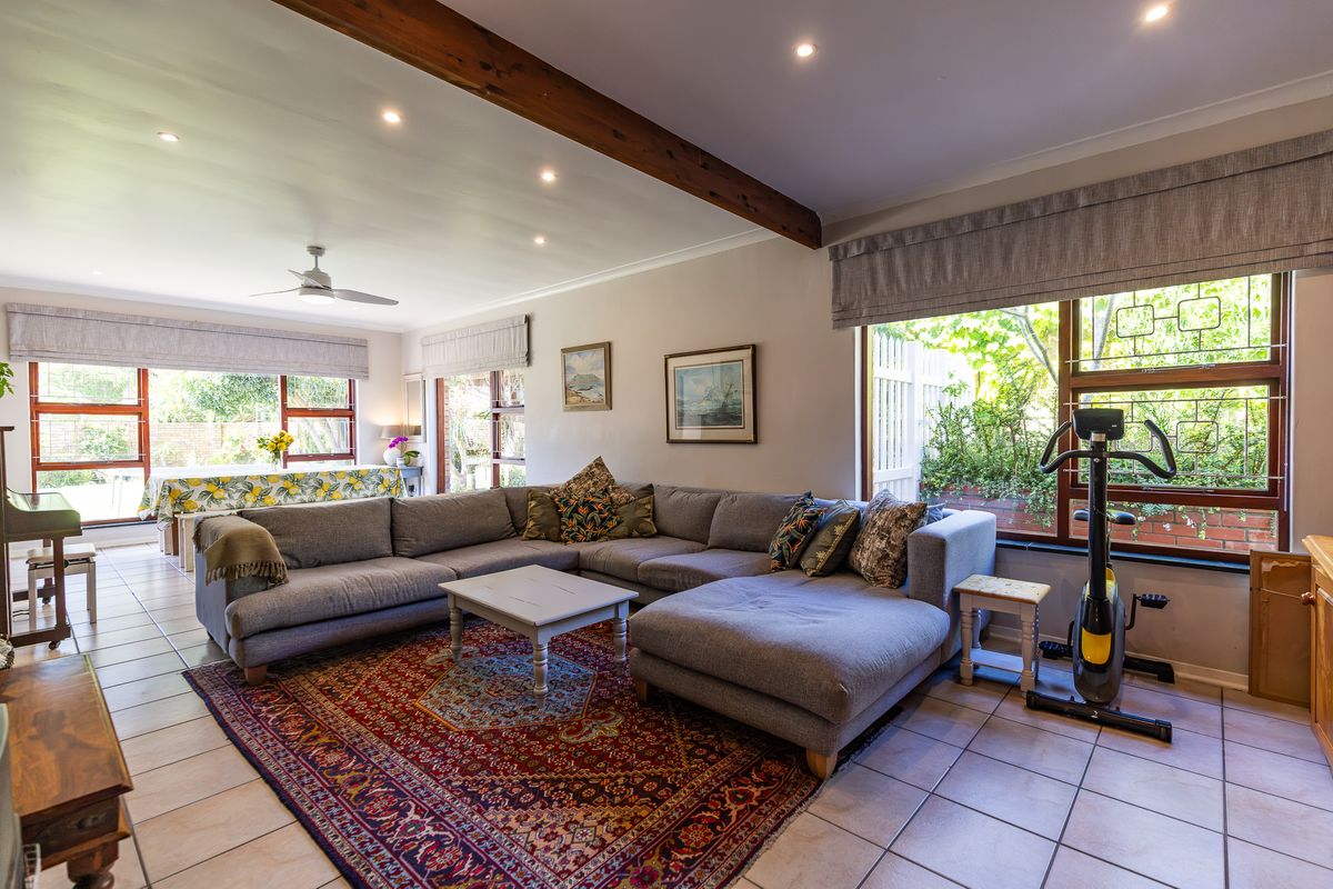 Spacious living room featuring tiled flooring, exposed timber ceiling beams, recessed lighting, and large windows providing ample natural light and garden access.