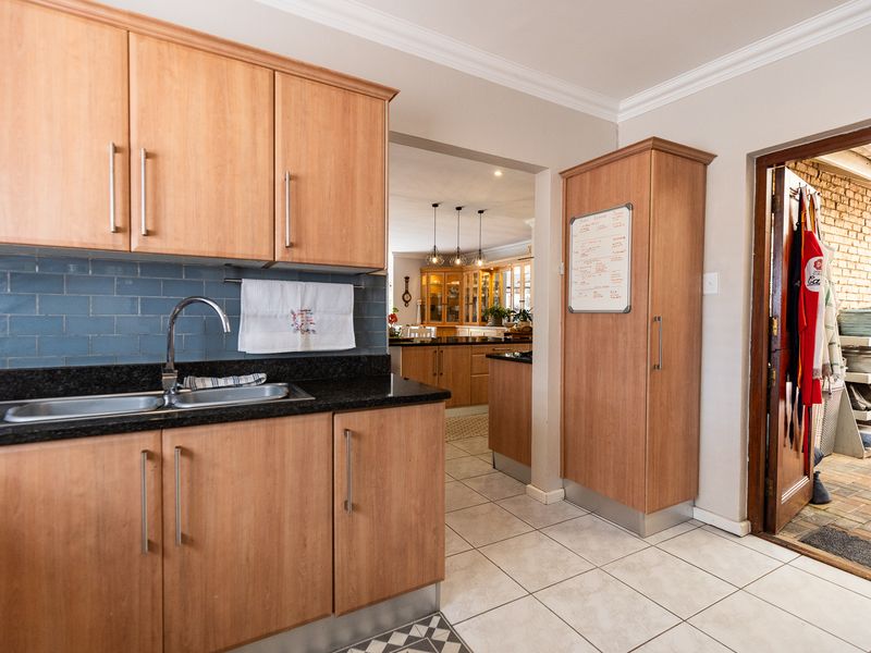 A functional kitchen featuring light wood cabinetry, granite countertops, a double basin sink, and a blue tiled backsplash, with an adjacent scullery area.