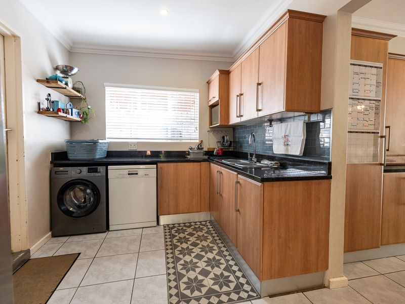 A functional scullery featuring laminate cabinetry, granite countertops, a stainless steel sink, and tiled flooring with a decorative inlay.