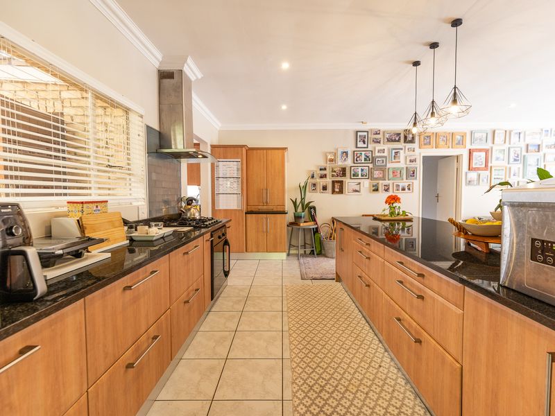 A well-appointed kitchen featuring granite countertops, warm wooden cabinetry, a gas hob with stainless steel extractor, and modern pendant lighting.