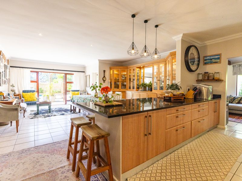 Spacious open-plan living area featuring a modern kitchen with a large island, granite countertops, wooden cabinetry, and seamless flow to the outdoor patio.