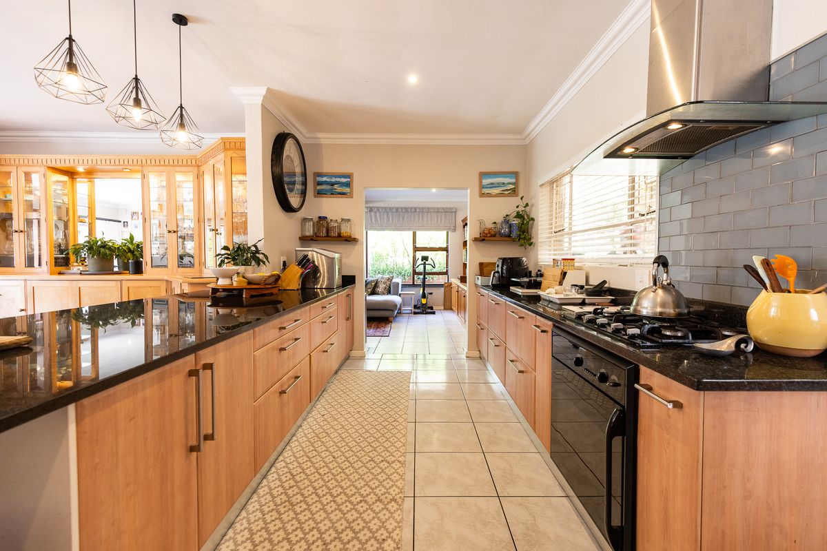 Spacious galley-style kitchen featuring light wood cabinetry, dark granite countertops, a gas hob with extractor fan, and a stylish subway tile backsplash.