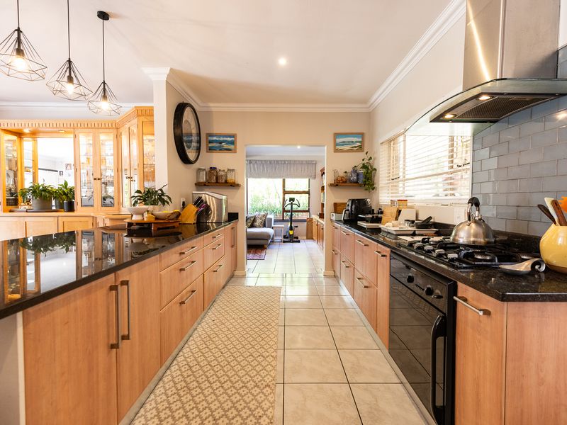 Spacious galley-style kitchen featuring light wood cabinetry, dark granite countertops, a gas hob with extractor fan, and a stylish subway tile backsplash.