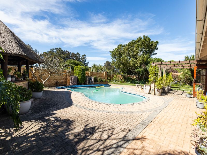 Outdoor entertainment area featuring a swimming pool, brick-paved patio, and a thatched lapa, perfect for summer relaxation and hosting guests.