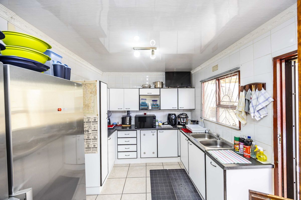A functional kitchen featuring white cabinetry, tiled walls, and a double stainless steel sink, offering a practical layout with ample storage space.
